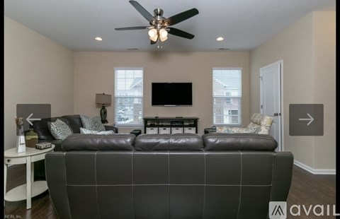A living room with a black couch and a ceiling fan.
