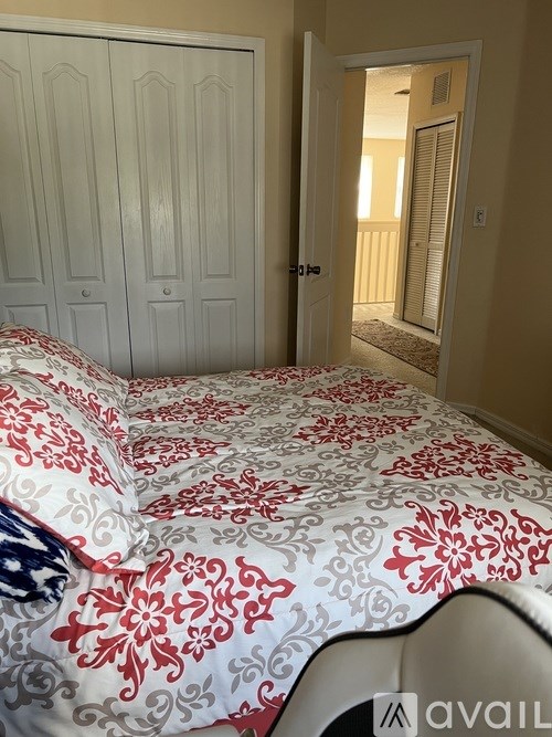 A bed with a red and white comforter is in a room with a white wardrobe and a doorway leading to another room.