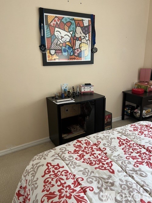 A bedroom with a bed, a framed picture on the wall, and a small table with a few items on it.