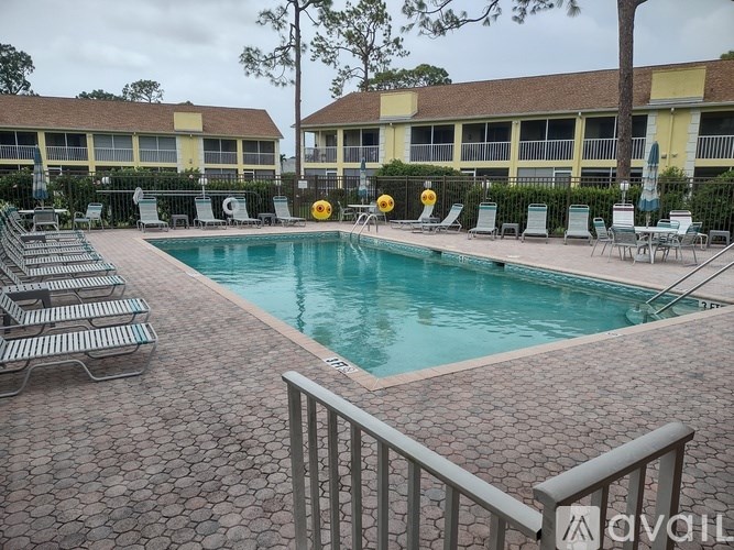 A pool surrounded by chairs and a building in the background.