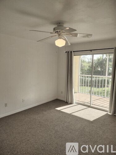 A room with a ceiling fan and sliding glass doors leading to a balcony.