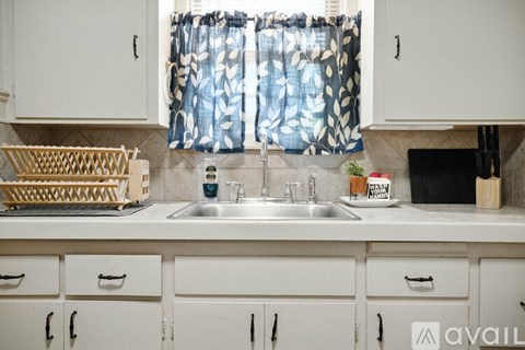 A kitchen with white cabinets and a window with a blue and white curtain.