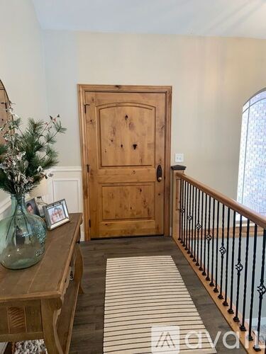 A wooden door with a glass panel is flanked by a wooden table with a vase and a framed picture on it.