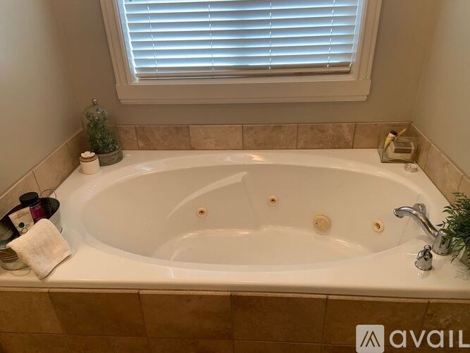 A white bathtub with a towel, candle, and soap on a tiled bathroom counter.