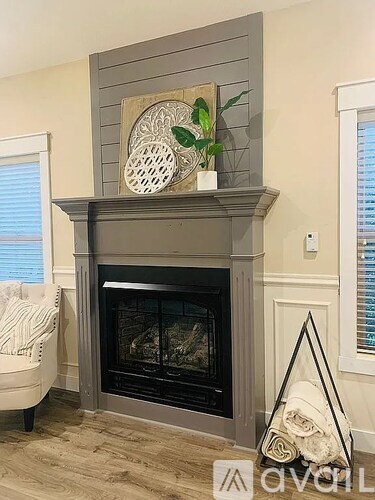 A grey fireplace with a plant on top and a white chair beside it.