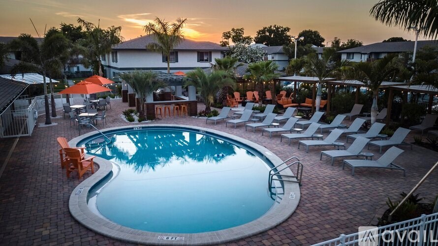 A swimming pool surrounded by lounge chairs and umbrellas at sunset.