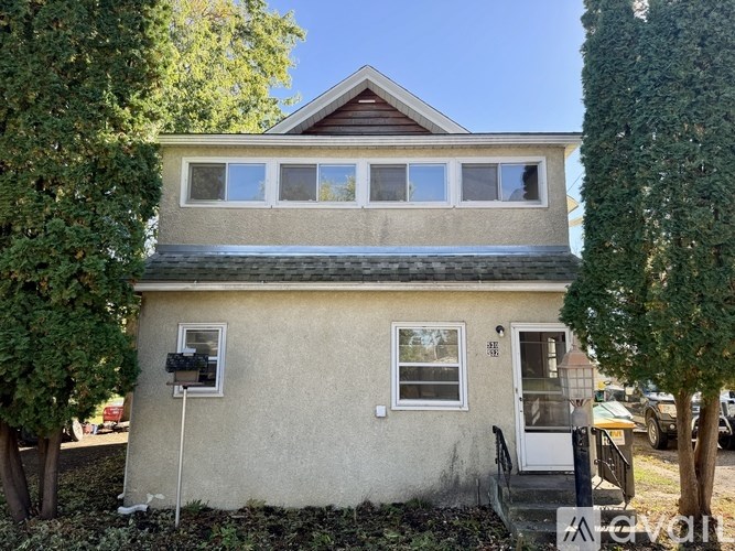 A small house with a brown roof and a white door is surrounded by trees.