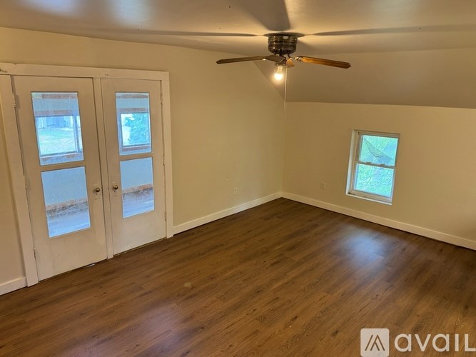 A room with a ceiling fan and two windows with doors.