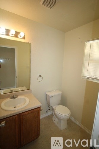 A bathroom with a toilet, sink, mirror and lights.