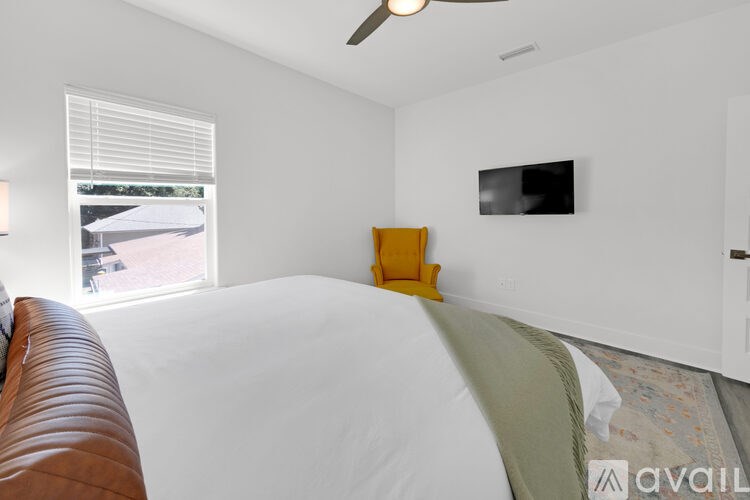 A bedroom with a bed, a brown leather chair, a ceiling fan, and a flat-screen TV mounted on the wall.