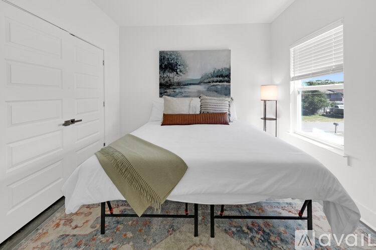 A bedroom with a white bed and a painting on the wall.