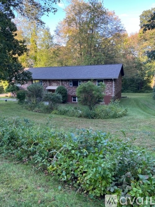 A red brick house with a grey roof surrounded by greenery.