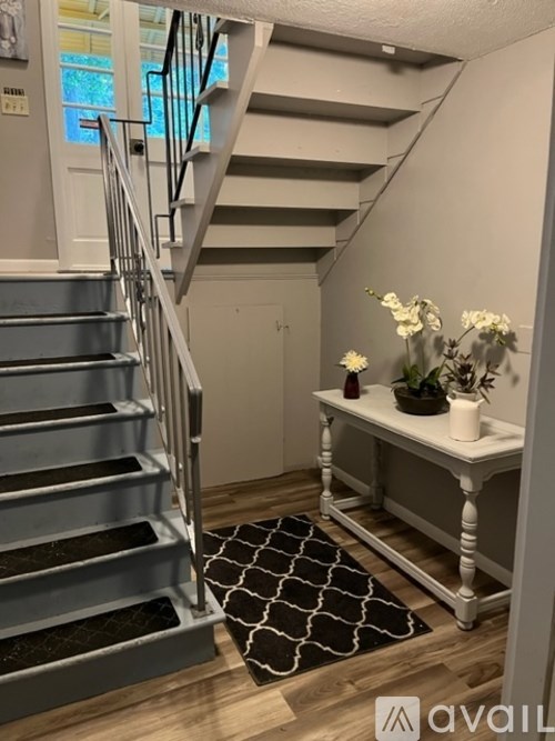 A staircase with a grey metal railing and a white bench with a vase of flowers on it.