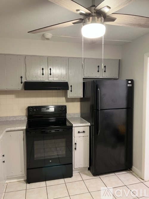 A black fridge and oven in a kitchen with white cabinets.