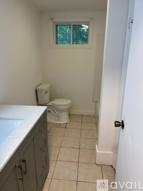 A bathroom with a toilet, sink, and a window.