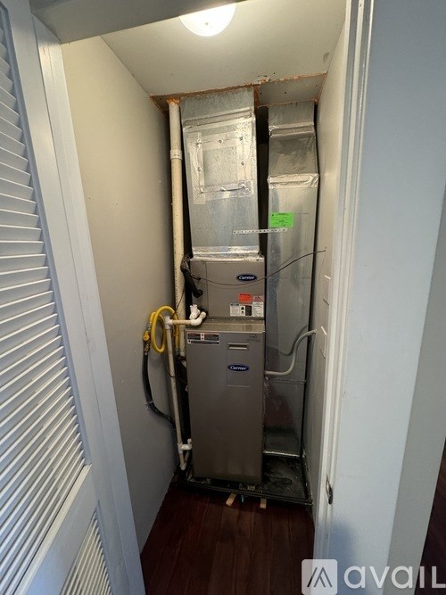 A small room with a stainless steel water heater and pipes.