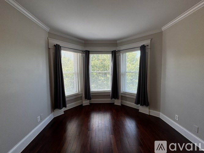 A room with wooden floors and a large window with curtains.