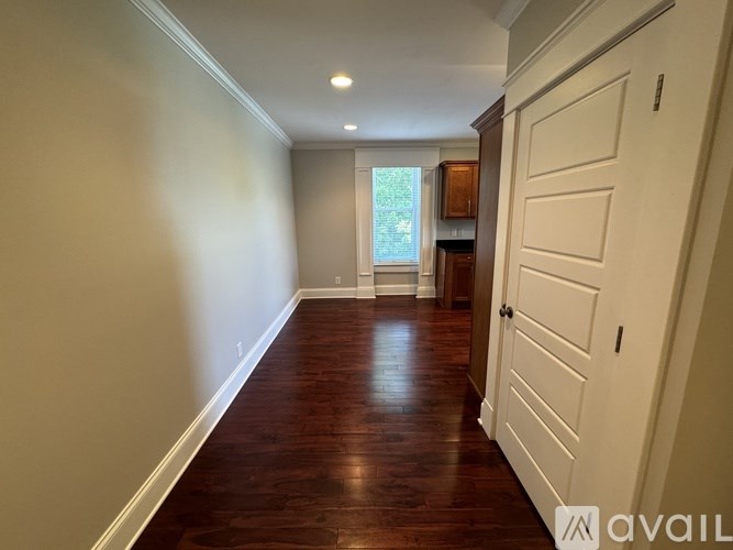 A hallway with wooden floors and white walls leading to a kitchen area.