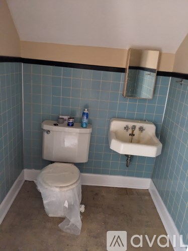A bathroom with a toilet, sink, and a trash bag on the floor.