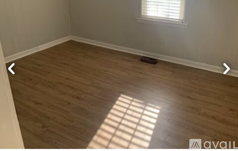 A room with wooden flooring and a window letting in sunlight.