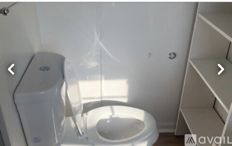 A white toilet with a white tank and a white shelf to the right.