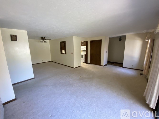 A spacious empty room with a ceiling fan and a door on the right side.