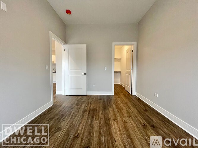A room with wooden floors and white walls, with a doorway leading to another room.