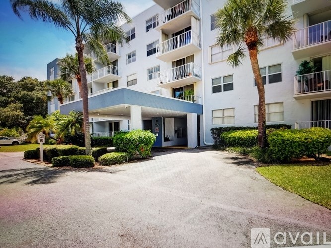 A white apartment building with balconies and palm trees in front.