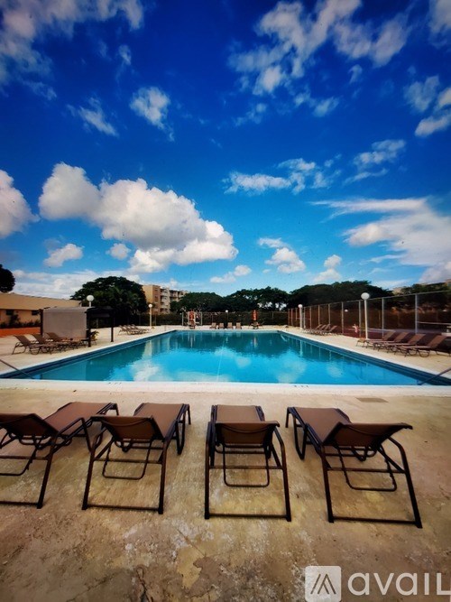 A pool with chairs and a blue sky with clouds.
