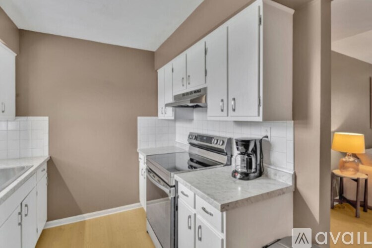 A kitchen with white cabinets and appliances, a countertop, and a small table with a lamp.