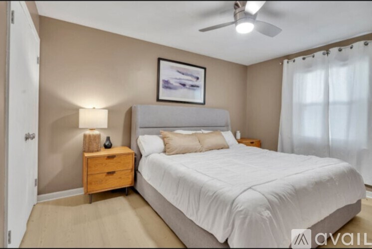 A bedroom with a large bed, a ceiling fan, and a nightstand with a lamp.