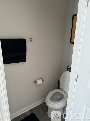 A white toilet in a small bathroom with a black towel hanging on the wall.
