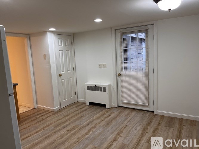 A room with wooden flooring and white walls, featuring a door with blinds and a small white radiator.