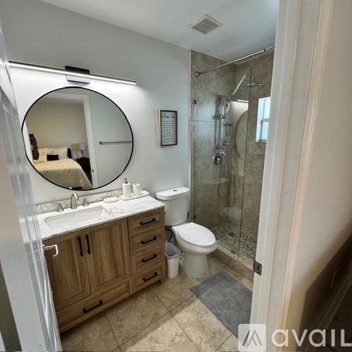 A bathroom with a round mirror, sink, toilet, and a walk-in shower.