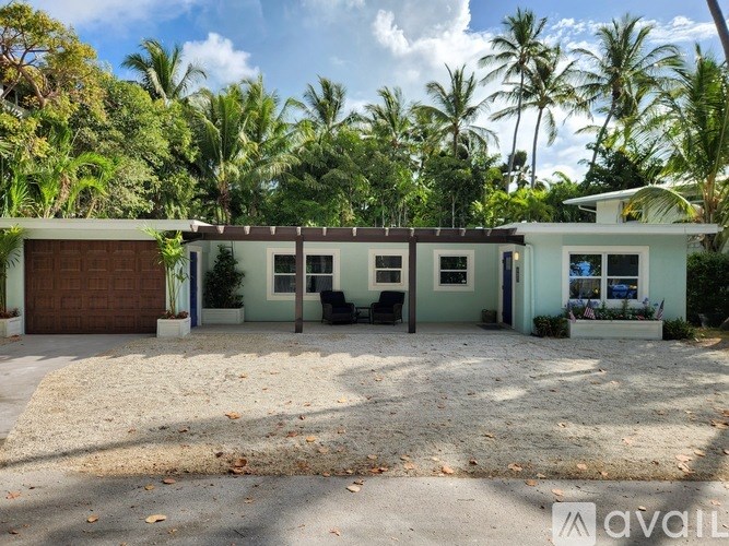 A house with a brown garage door is surrounded by palm trees.