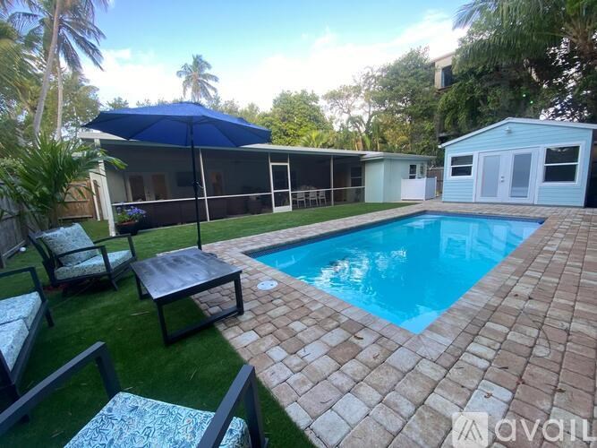 A pool surrounded by a brick patio and a blue umbrella.
