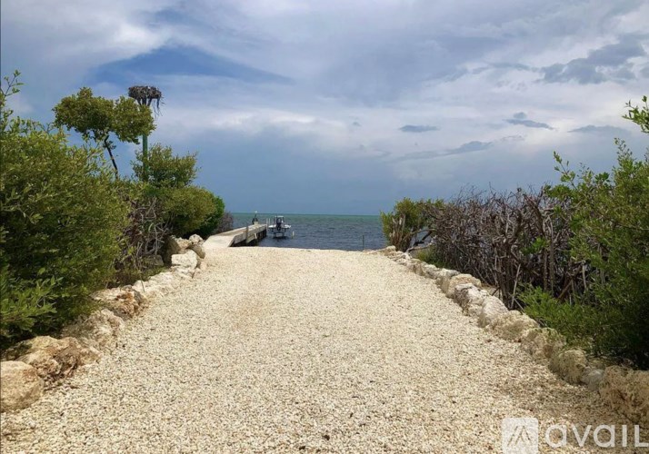 A gravel path leads to a body of water with a boat in the distance.