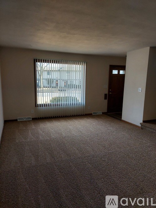 A room with a carpeted floor and a window with blinds.