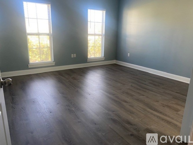 A room with wooden flooring and two windows.