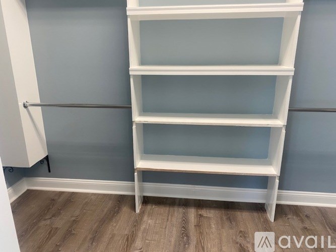 A white shelving unit with four shelves stands against a grey wall.