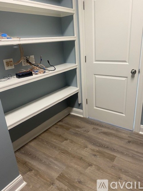 A white door is on the right side of a hallway with shelves on the left.