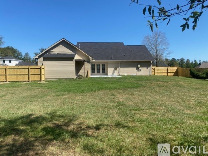 A house with a grey roof and a brown fence is surrounded by a grassy area.