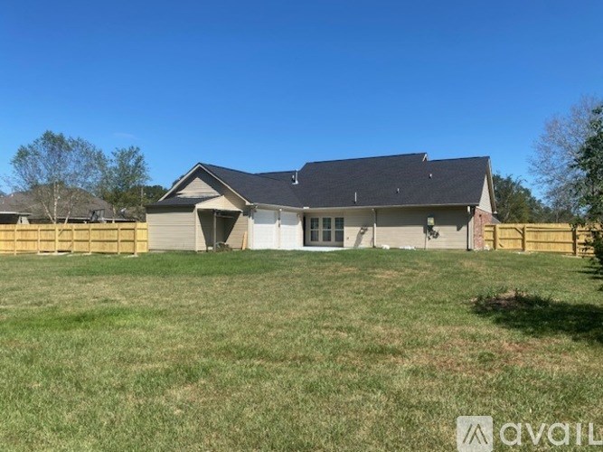 A house with a grey roof and a white garage door is surrounded by a fence and green grass.