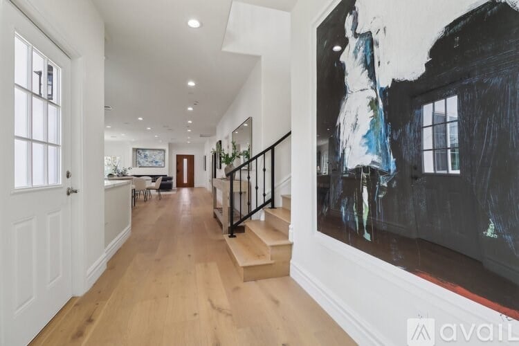 A hallway with a large painting on the wall and a staircase.