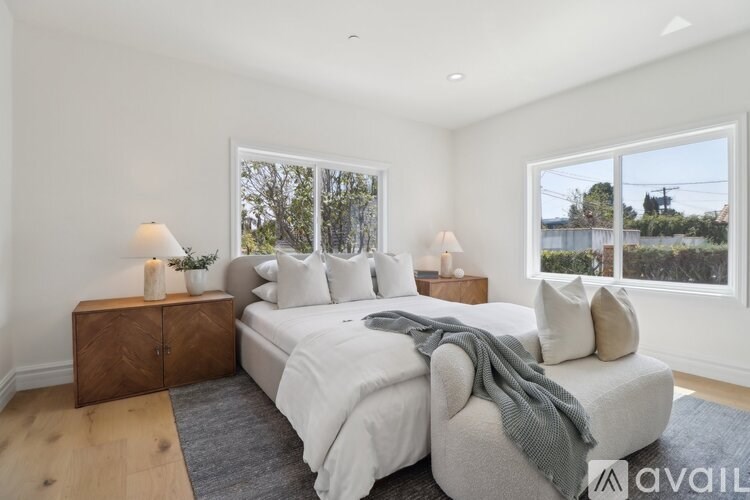 A bedroom with a large bed, two nightstands, and a window overlooking a fence.