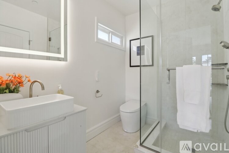 A bathroom with a white sink, toilet, and a glass shower stall.