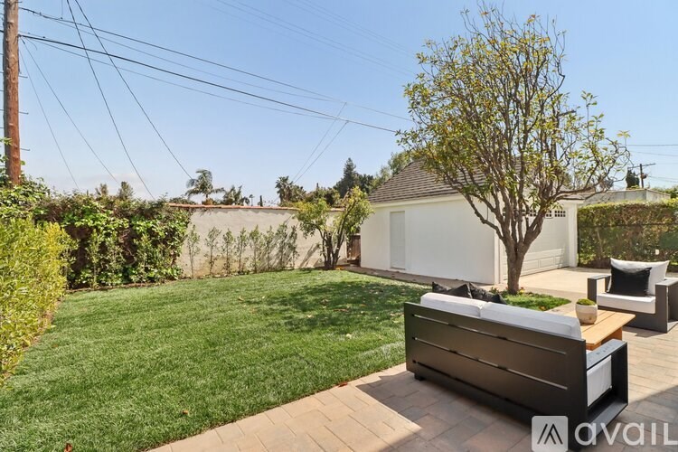 A backyard with a bench, a tree, and a house in the background.