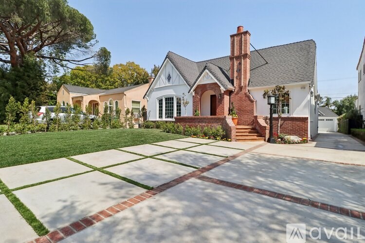 A house with a brick chimney and a white facade is surrounded by a well-manicured lawn.