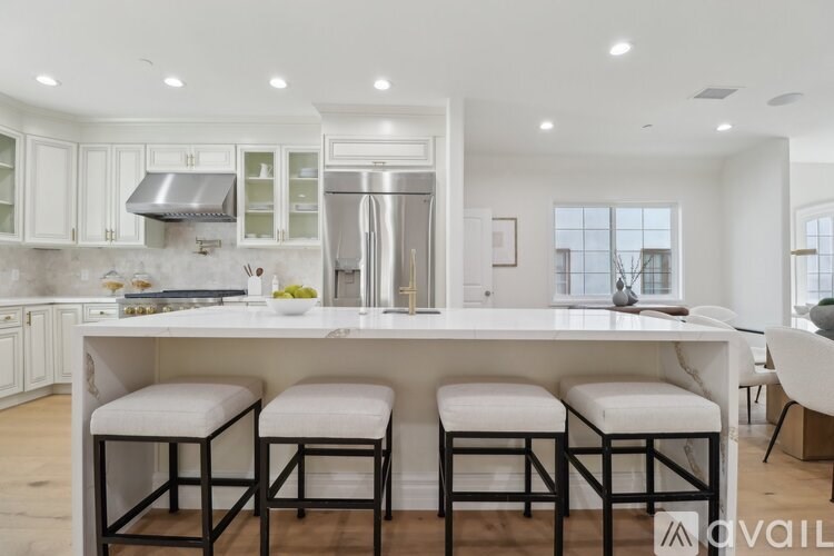 A kitchen with white cabinets and a large island with bar stools.