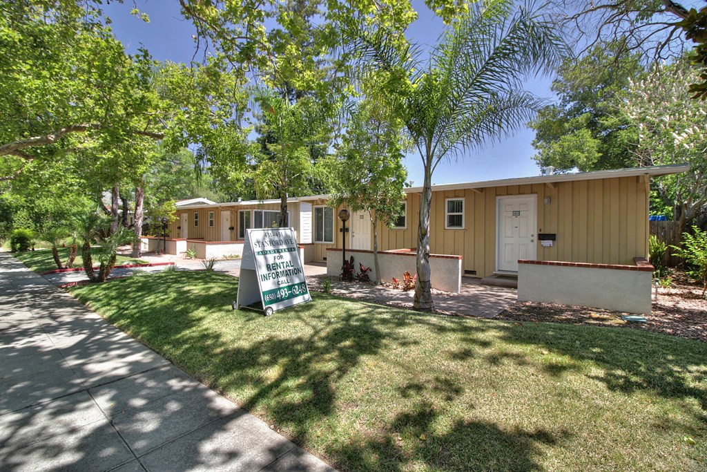 A sign in front of a house with a tree in front of it.